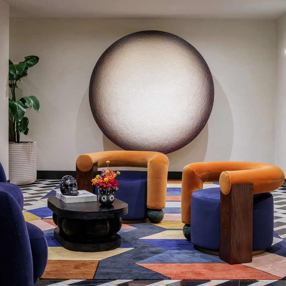 Two Galatea armchairs with blue velvet and orange backs, smoked walnut wood, and Verde Guatemala marble at The Moore Hotel.