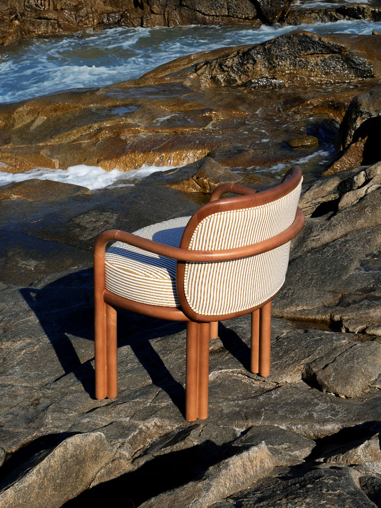 James dining chair in oak and striped fabric on top of rocks next to the sea.
