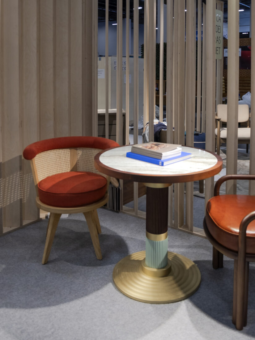 Queens dining table and George dining chair Queens Dining Table with a marble top, a single smoked walnut wood leg featuring lacquered detail and brushed brass accents, paired with a George Dining Chair in oak and orange fabric.