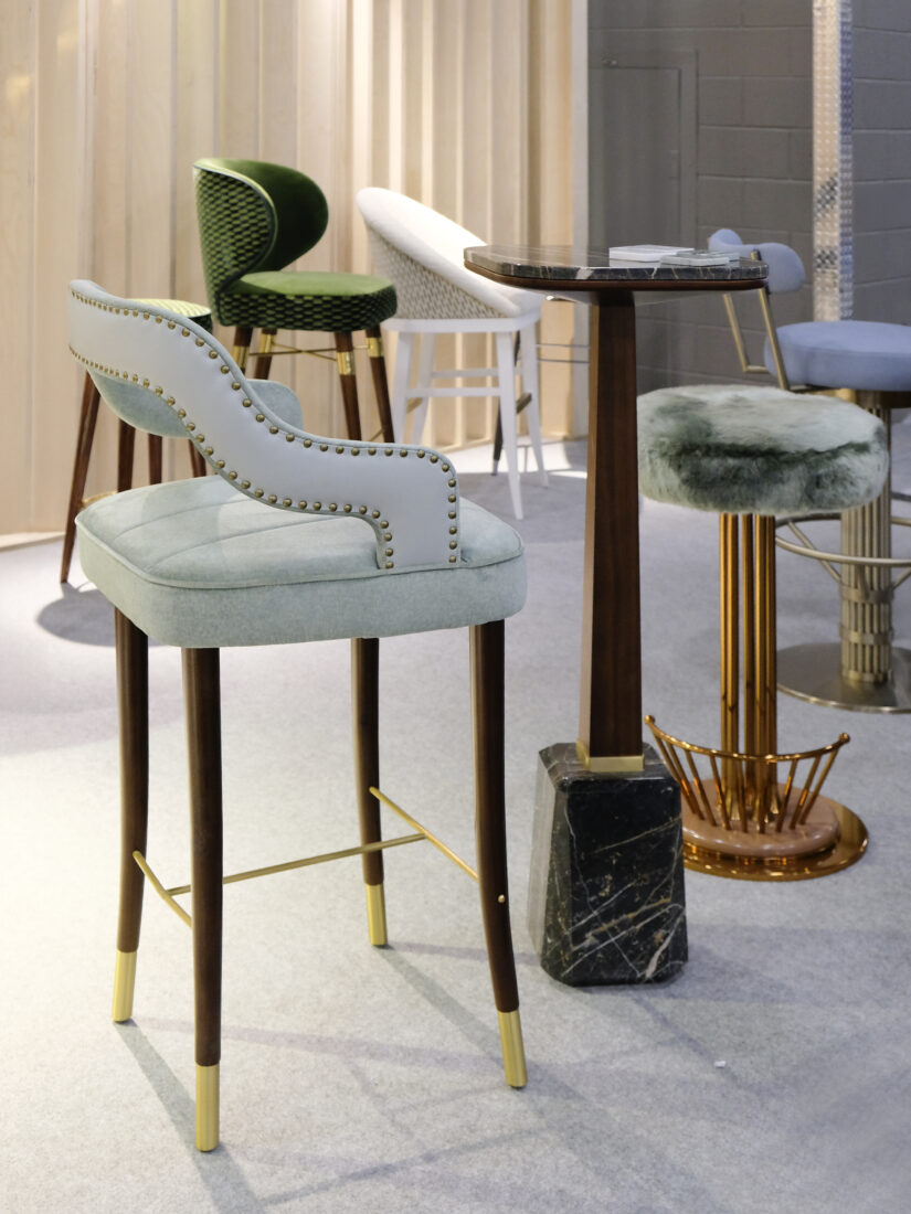 Kelly Bar Chair, Oakland Bar Table and Andy Bar Stool Kelly Bar Chair in baby blue fabric with walnut wood legs and polished brass accents, next to the Oakland Bar Table with a marble top and the Andy Bar Stool featuring a fur seat and copper structure