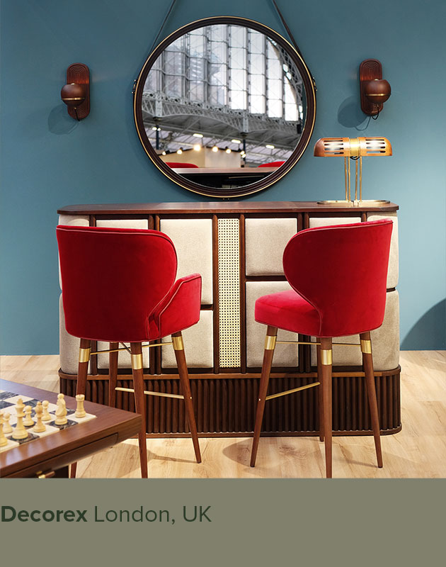 Louis I Chair and Louis Bar Chair upholstered in red velvet with smoked walnut legs and brass details, displayed alongside the Tom Bar Counter, Reynolds Mirror, Turing Table Lamp, and Fleming Wall Lamp at Decorex London.
