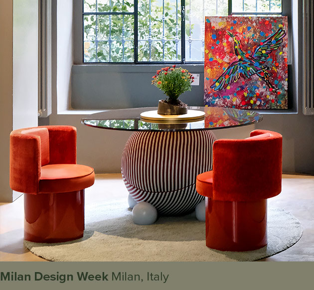 Two Myth dining chairs in orange placed next to the Circulus dining table, upholstered in striped fabric with sphere feet, displayed at Milan Design Week.