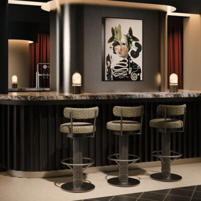 Bar setting by Porus featuring the Willis Bar Chair upholstered in luxurious patterned green fabric, accompanied by the Russell Table Lamp with marble and alabaster.