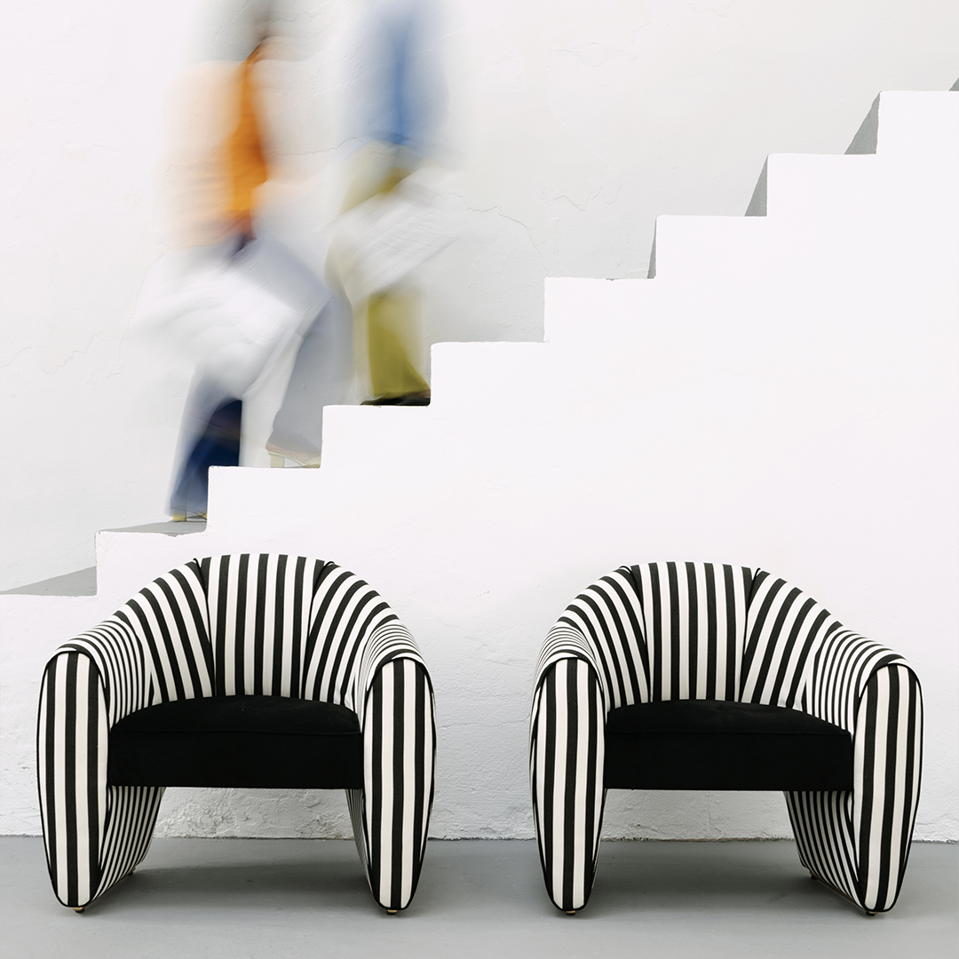 Viginti XX Armchair Two Viginti XX armchairs upholstered in striped black and white fabric, placed near a staircase with two out-of-focus figures ascending.